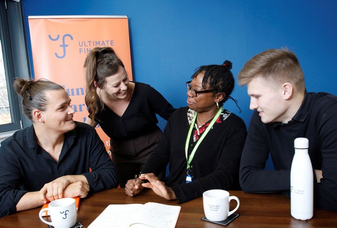 Four Ultimate Finance employees having a conversation at a desk in a meeting room in the Bristol office